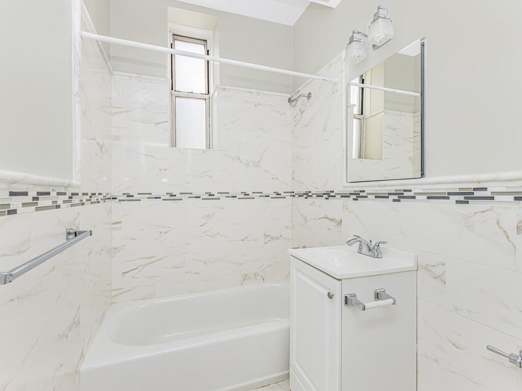 Newly renovated bathroom with white tile and fixtures and a gray and black glass tile accent